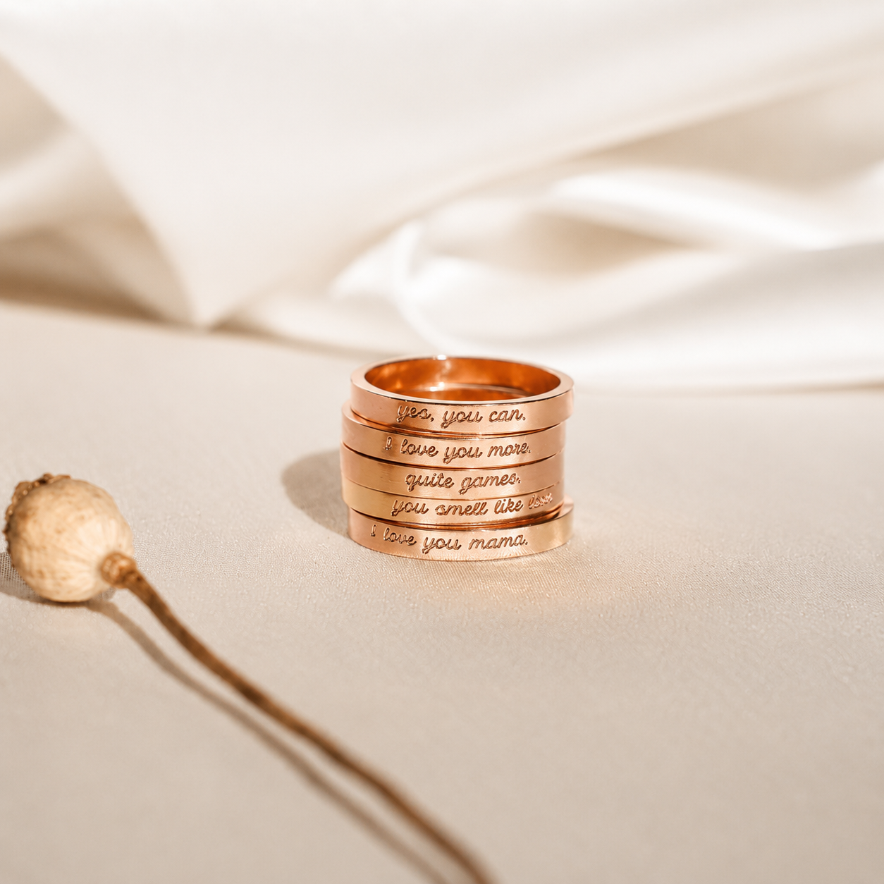 Stack of rose gold rings with engraved text on a beige fabric background
